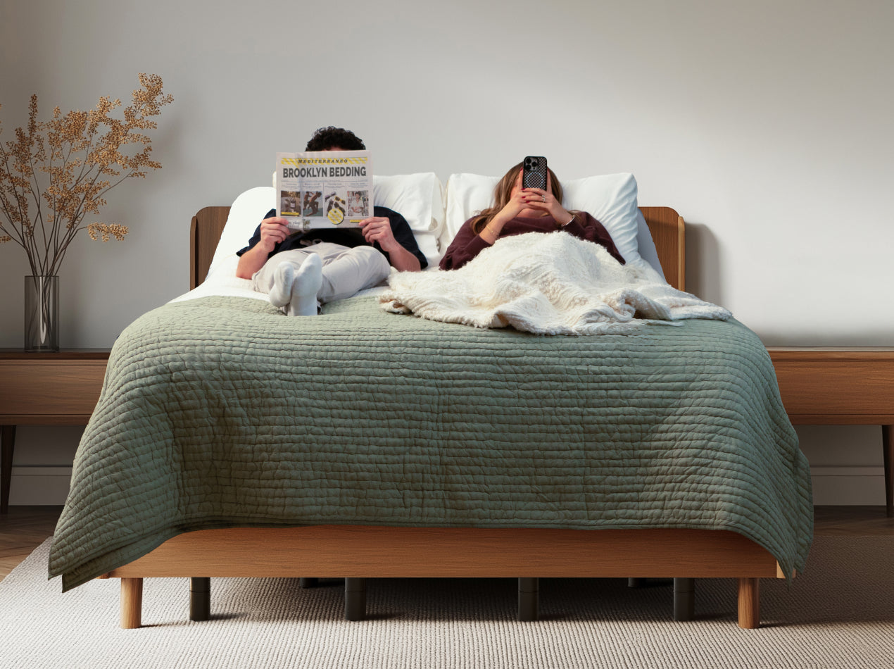Two people relaxing on a bed with the Ascension® Ultra Adjustable Power Base, with one person reading and the other using a phone.